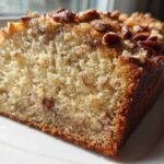 Close-up of a moist slice of sweet alabama pecan bread topped with toasted pecans, sitting on a white plate.