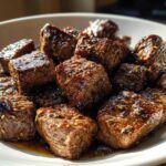 Close-up of tender, seasoned cubes of crockpot steak resting in a white bowl with savory juices.