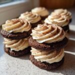Close-up of stacked chocolate tiramisu cookies filled with cream frosting and dusted with cocoa powder.