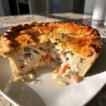 A cross-section view of a golden-crusted turkey pot pie recipe, showing creamy filling with shredded turkey and vegetables.