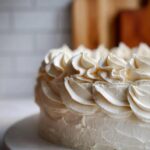 Close-up of a cake generously frosted with perfectly piped swirls of creamy vanilla buttercream.