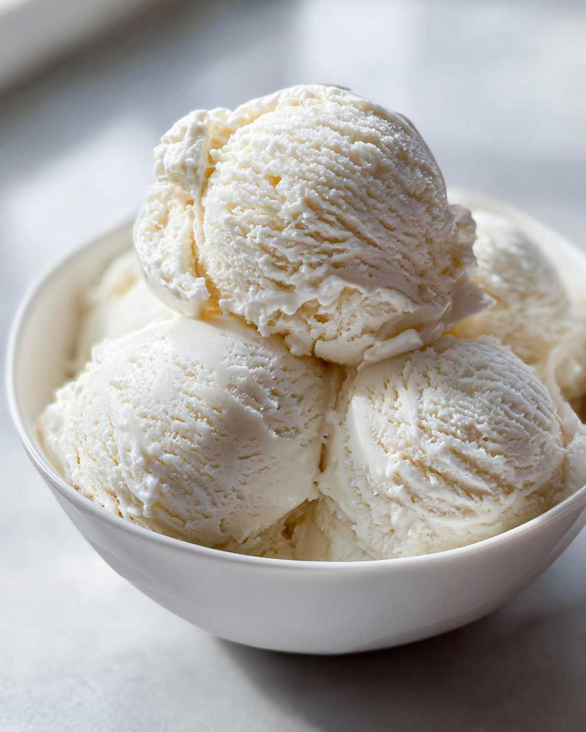 Close-up of several scoops of creamy white protein ice cream piled high in a white bowl.