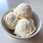 Three generous scoops of creamy white protein ice cream served in a simple white bowl.