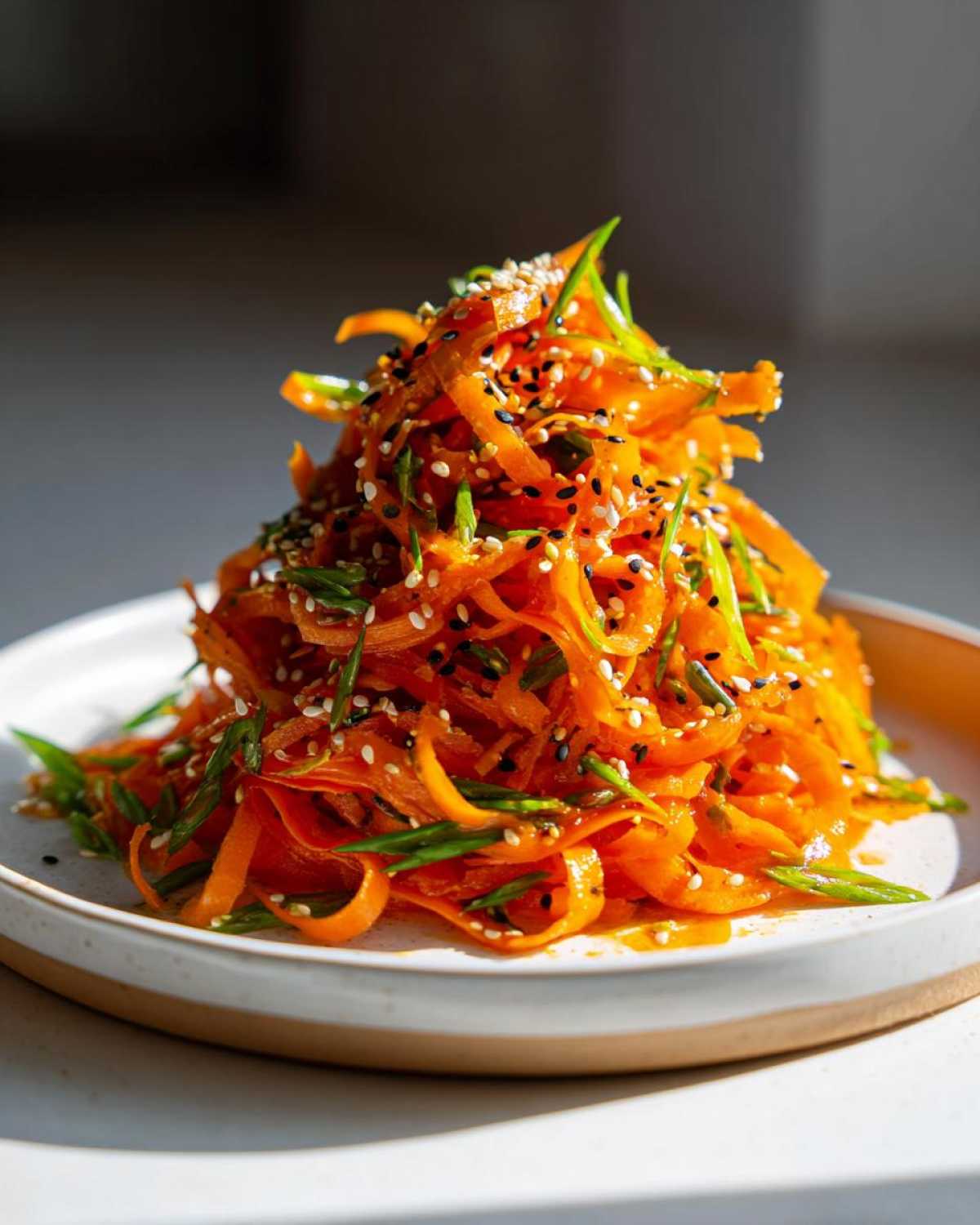 Close-up of a mound of bright orange raw carrot salad, garnished with green onions and sesame seeds.