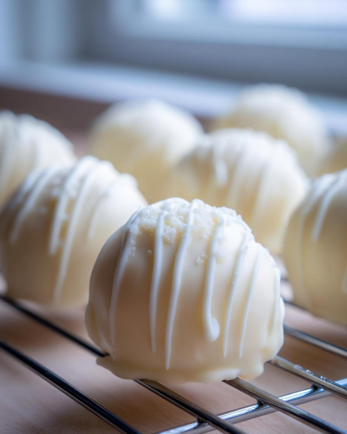 Close-up of a white chocolate coated sugar cookie truffle drizzled with white icing, resting on a cooling rack.