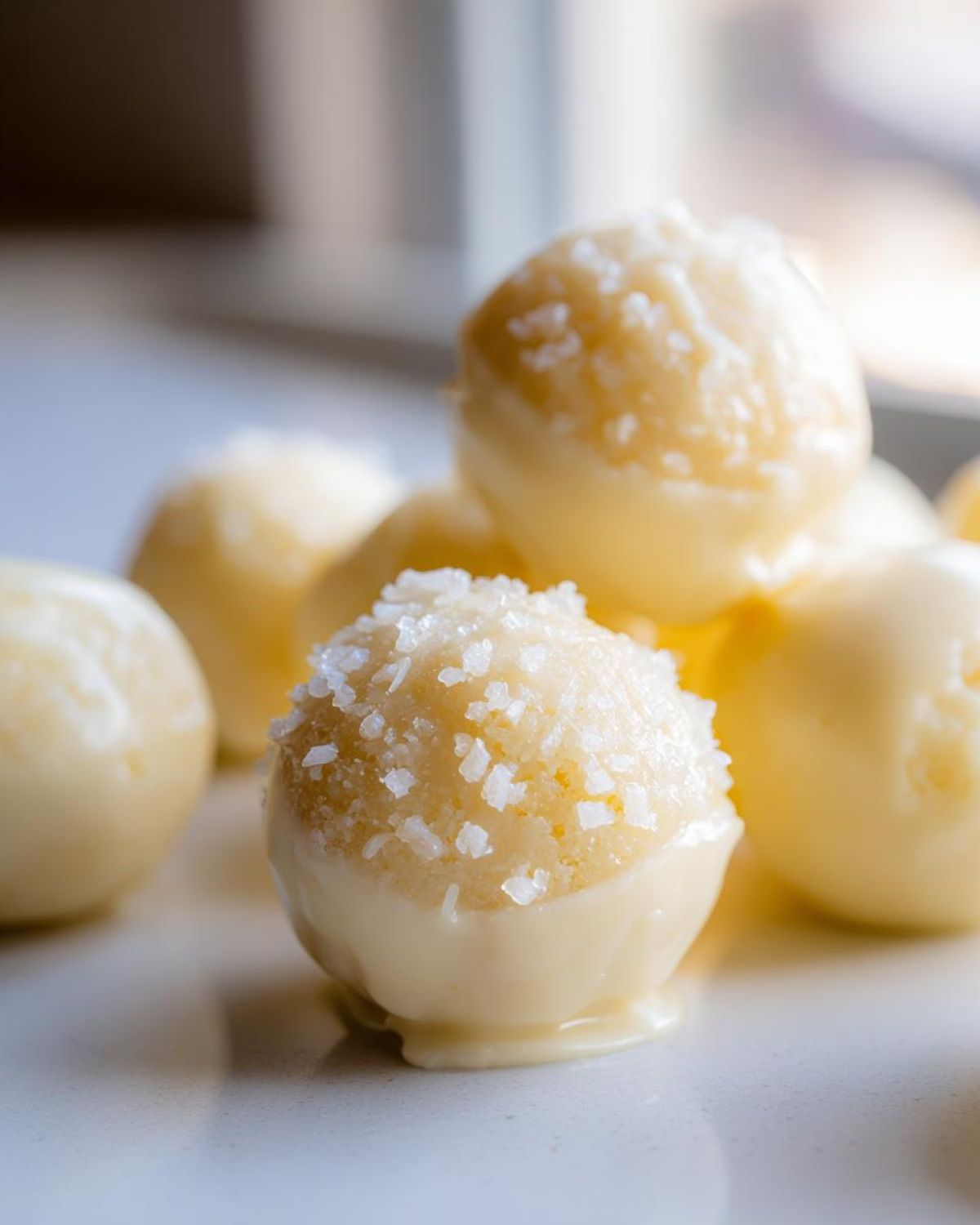 A close-up of white chocolate sugar cookie truffles dipped in frosting and topped with coarse salt crystals.