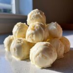 A stack of decadent white chocolate coated sugar cookie truffles sprinkled with cookie crumbs.