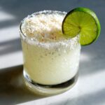 A chilled white Christmas margarita garnished with toasted coconut flakes and a fresh lime wheel.