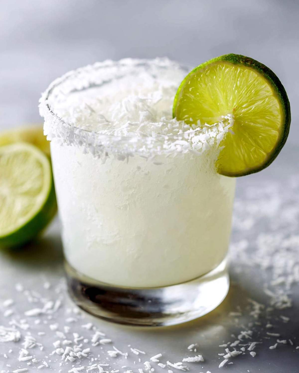 Close-up of a frosty white christmas margarita garnished with a lime wheel and shredded coconut rim.