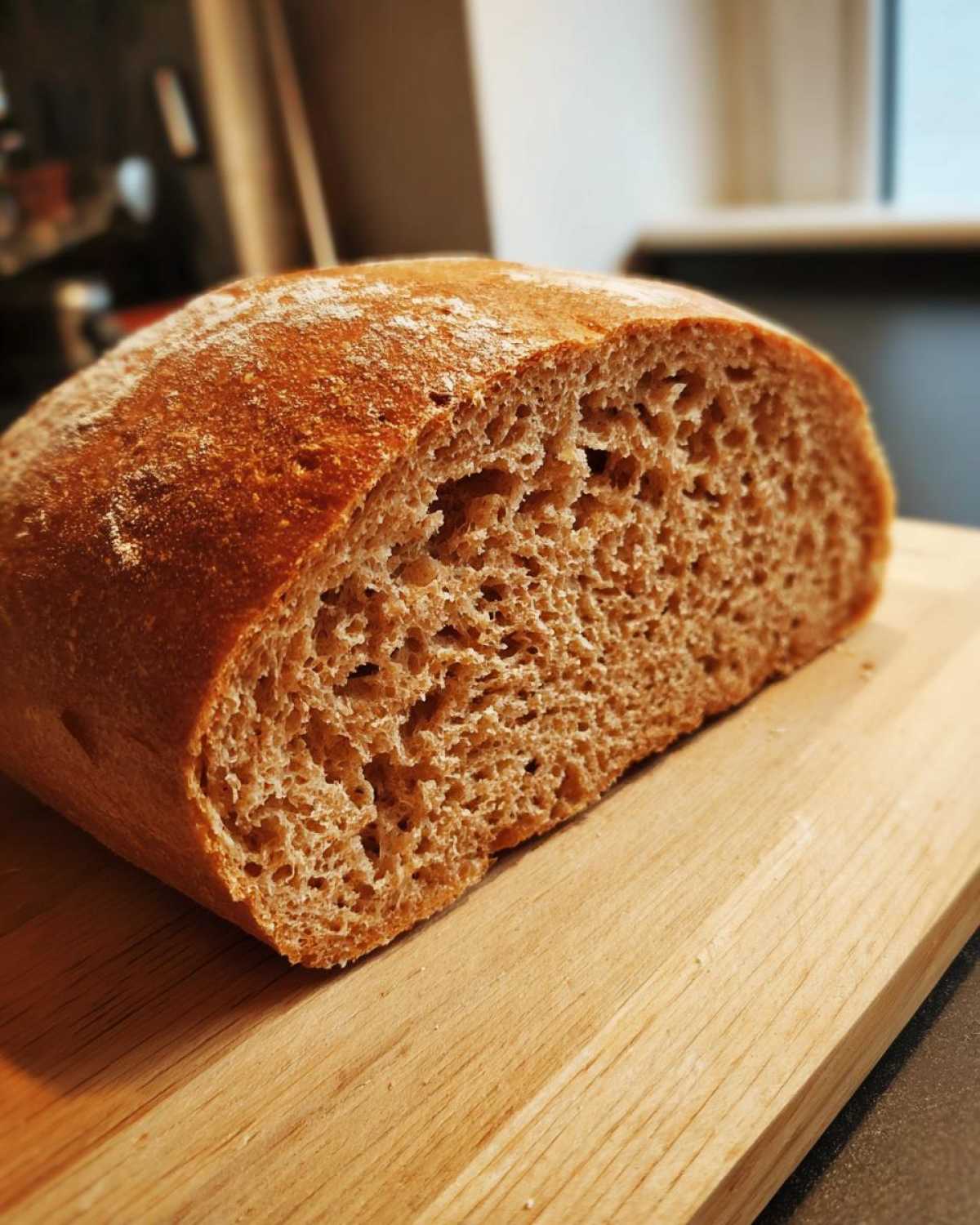 Close-up of the interior crumb structure of a freshly baked loaf of whole wheat bread on a wooden cutting board.