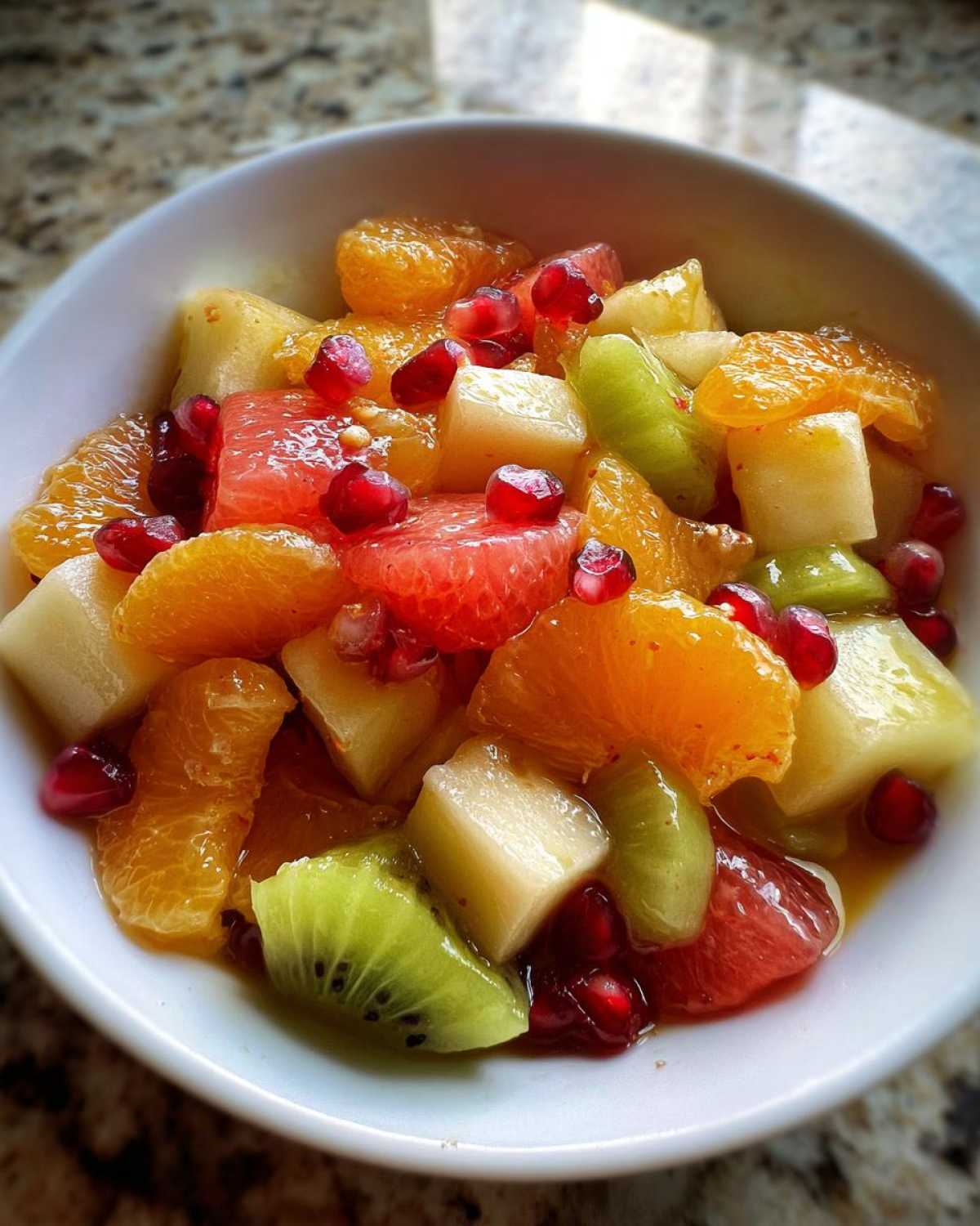Close-up of a vibrant winter fruit salad featuring oranges, kiwi, grapefruit, and pomegranate seeds in a white bowl.