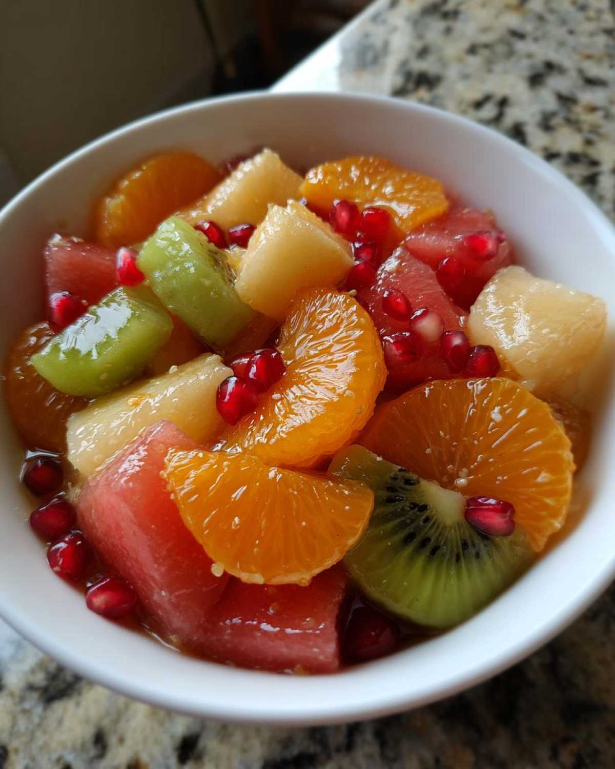 Close-up of a vibrant winter fruit salad featuring oranges, kiwi, watermelon, and pomegranate seeds in a white bowl.