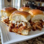Close-up of melted cheese oozing over shredded chicken filling in soft rolls for amazing bbq chicken sliders.