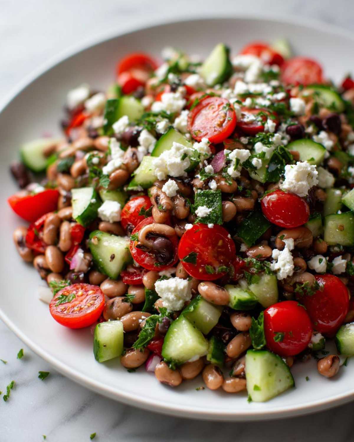 A vibrant close-up of a fresh bean salad featuring black-eyed peas, cherry tomatoes, cucumber chunks, and feta cheese.