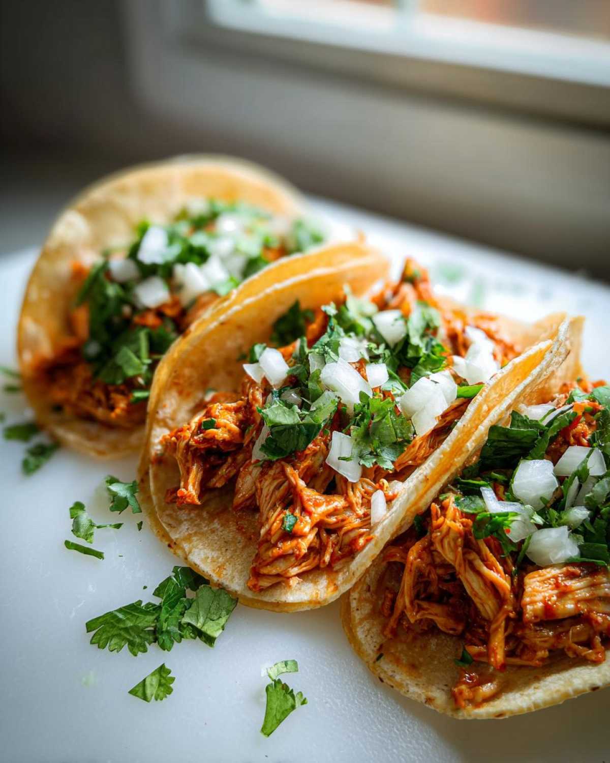 Three freshly made chicken tacos filled with shredded seasoned chicken, topped with diced white onion and fresh cilantro.