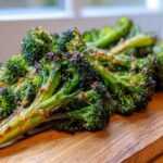 Close-up of perfectly seasoned and charred roasted broccoli florets resting on a wooden cutting board.