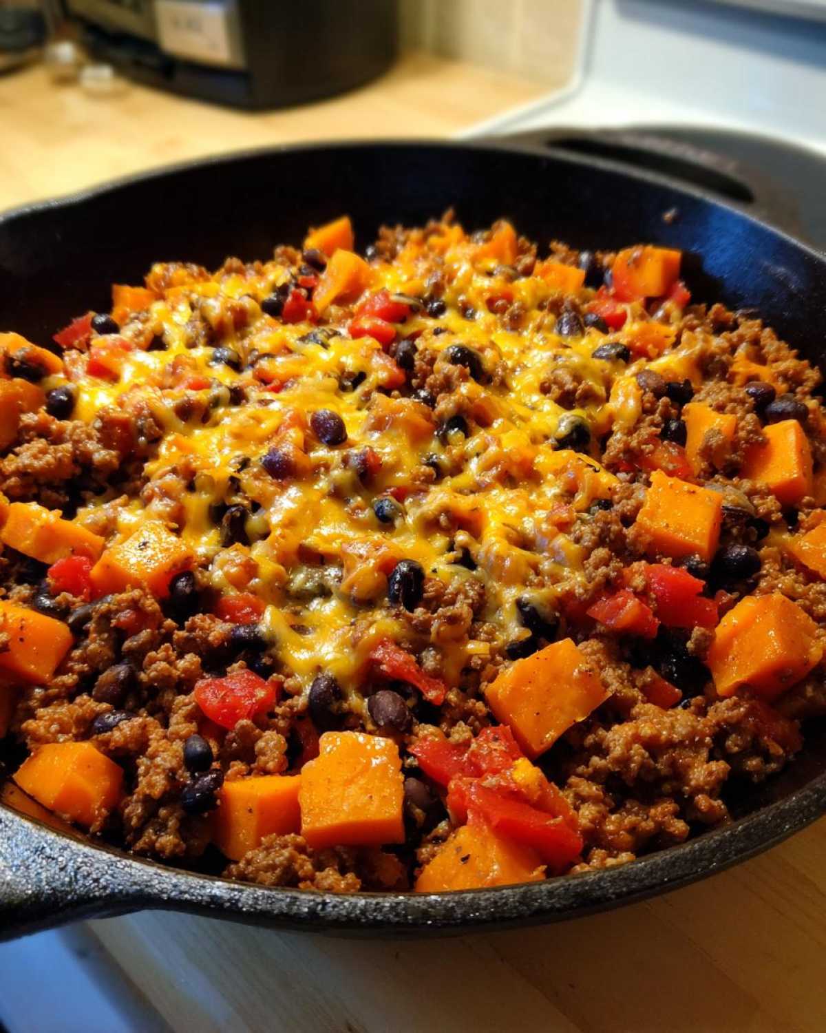 Close-up of a hearty sweet potato skillet featuring ground meat, black beans, diced tomatoes, and melted cheddar cheese.
