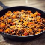 Close-up of a savory sweet potato skillet with ground meat, black beans, and melted cheese in a cast iron pan.