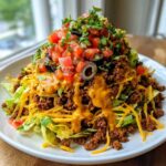 A tall, appetizing serving of taco salad featuring seasoned ground beef, shredded lettuce, cheese, and a generous topping of salsa and black olives.