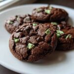 Four rich, dark chocolate Andes mint cookies studded with green mint pieces and chocolate chips on a white plate.