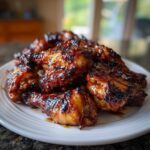 A pile of sticky, dark-glazed Authentic Huli Huli Chicken wings on a white plate.