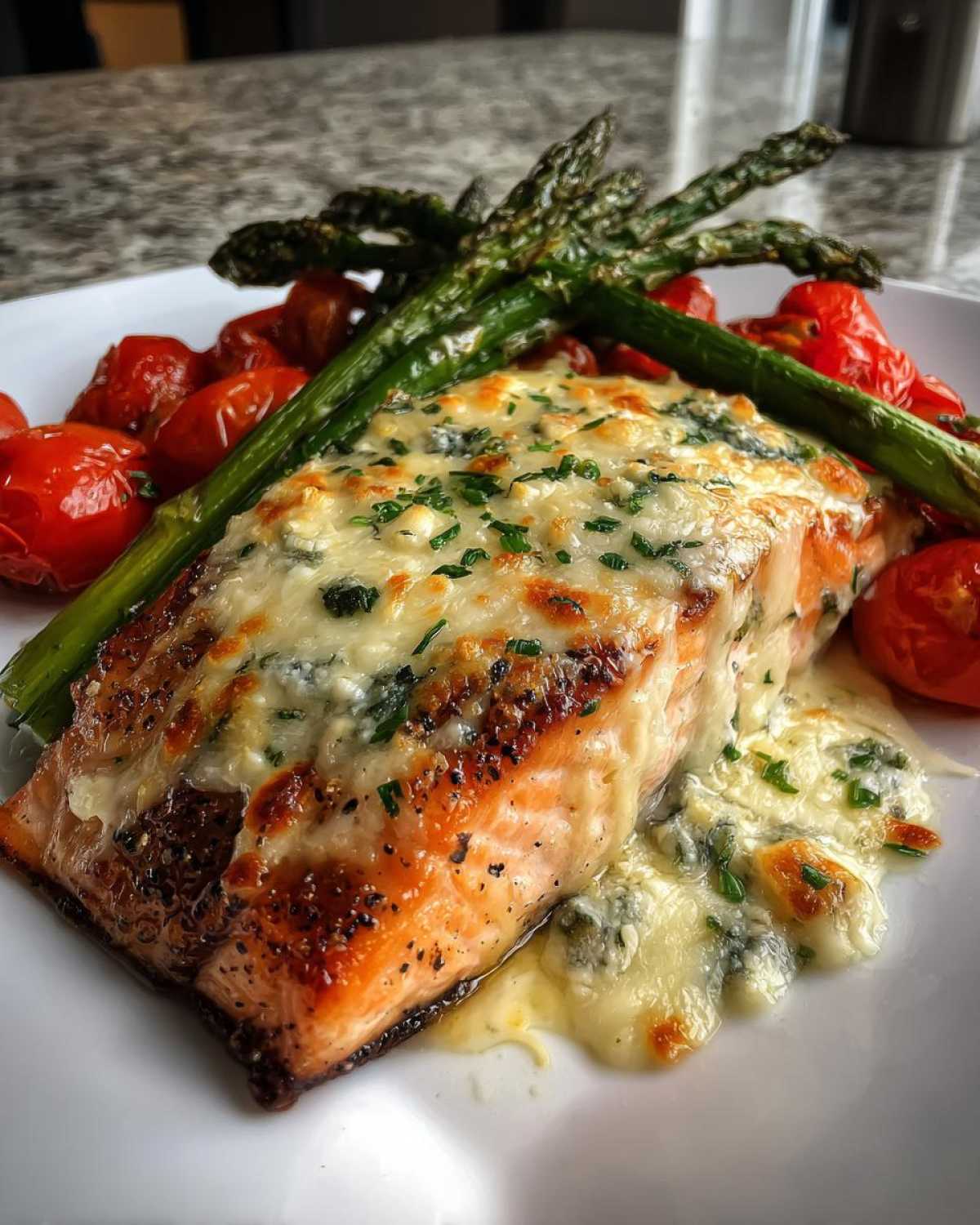 A perfectly cooked fillet of Baked Boursin Salmon topped with melted cheese and herbs, served with roasted asparagus and cherry tomatoes.