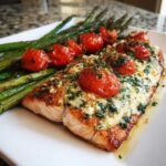 Close-up of a perfectly cooked Baked Boursin Salmon fillet topped with creamy Boursin cheese, herbs, and roasted cherry tomatoes, served with asparagus.