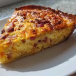 A close-up slice of Baked Hash Brown Quiche showing a golden, cheesy top and hash brown crust filled with eggs and bacon.