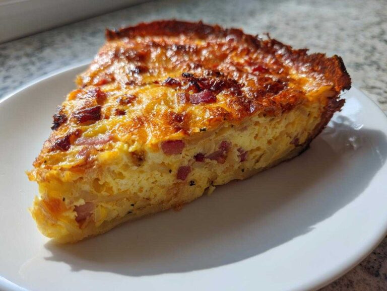 A close-up slice of Baked Hash Brown Quiche showing a golden, cheesy top and hash brown crust filled with eggs and bacon.