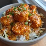Close-up of a Bang Bang Salmon Bites Bowl featuring crispy salmon bites coated in spicy sauce over rice and slaw, topped with sesame seeds.