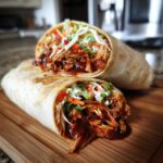 Two halves of a Bbq Chicken Wraps Flavorful Busy triumph, showing shredded chicken drenched in BBQ sauce and topped with coleslaw.