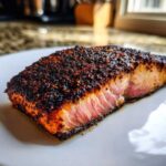 Close-up of a thick, perfectly cooked blackened salmon fillet showing a dark, spiced crust and pink, flaky interior.