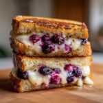 Close-up of two halves of a Blueberry Grilled Cheese sandwich stacked, showing melted cheese and bursting blueberries.