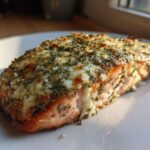 A close-up of a cooked salmon fillet topped with melted Boursin cheese and dried herbs.