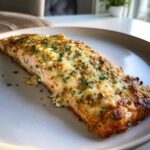 A close-up of a baked Boursin Salmon fillet topped with melted, golden cheese and fresh parsley.