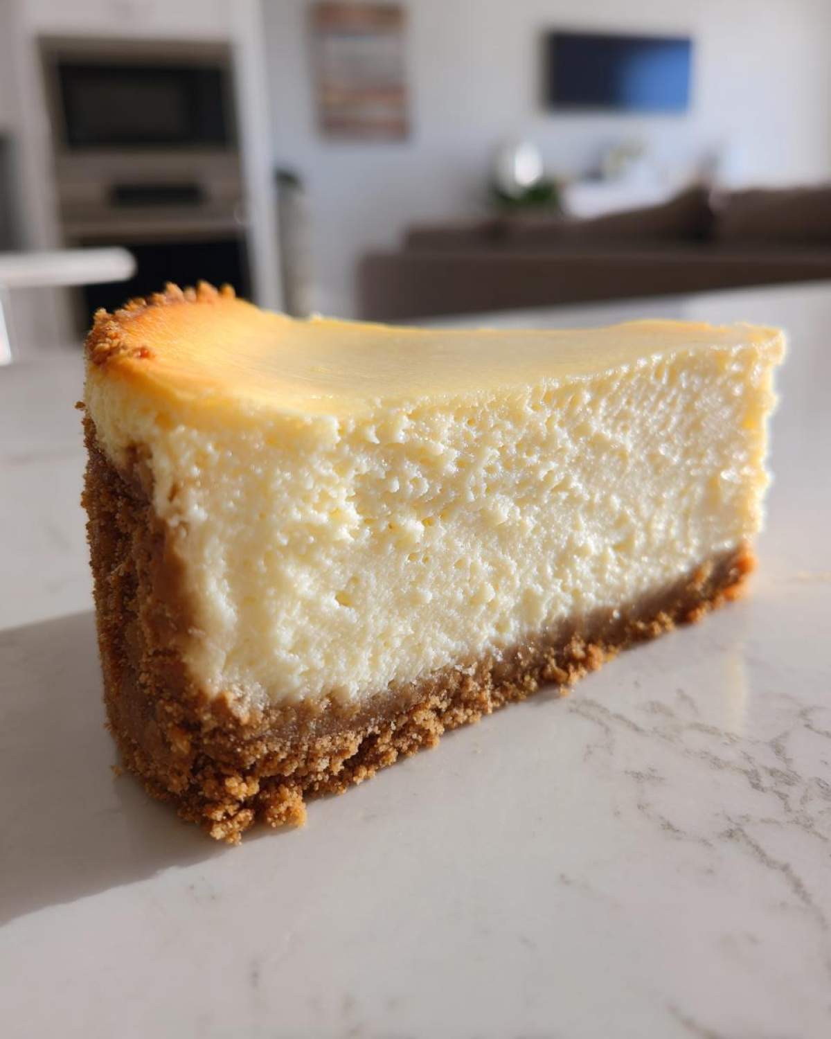 A close-up of a perfectly baked slice of creamy cheesecake recipe on a marble counter.