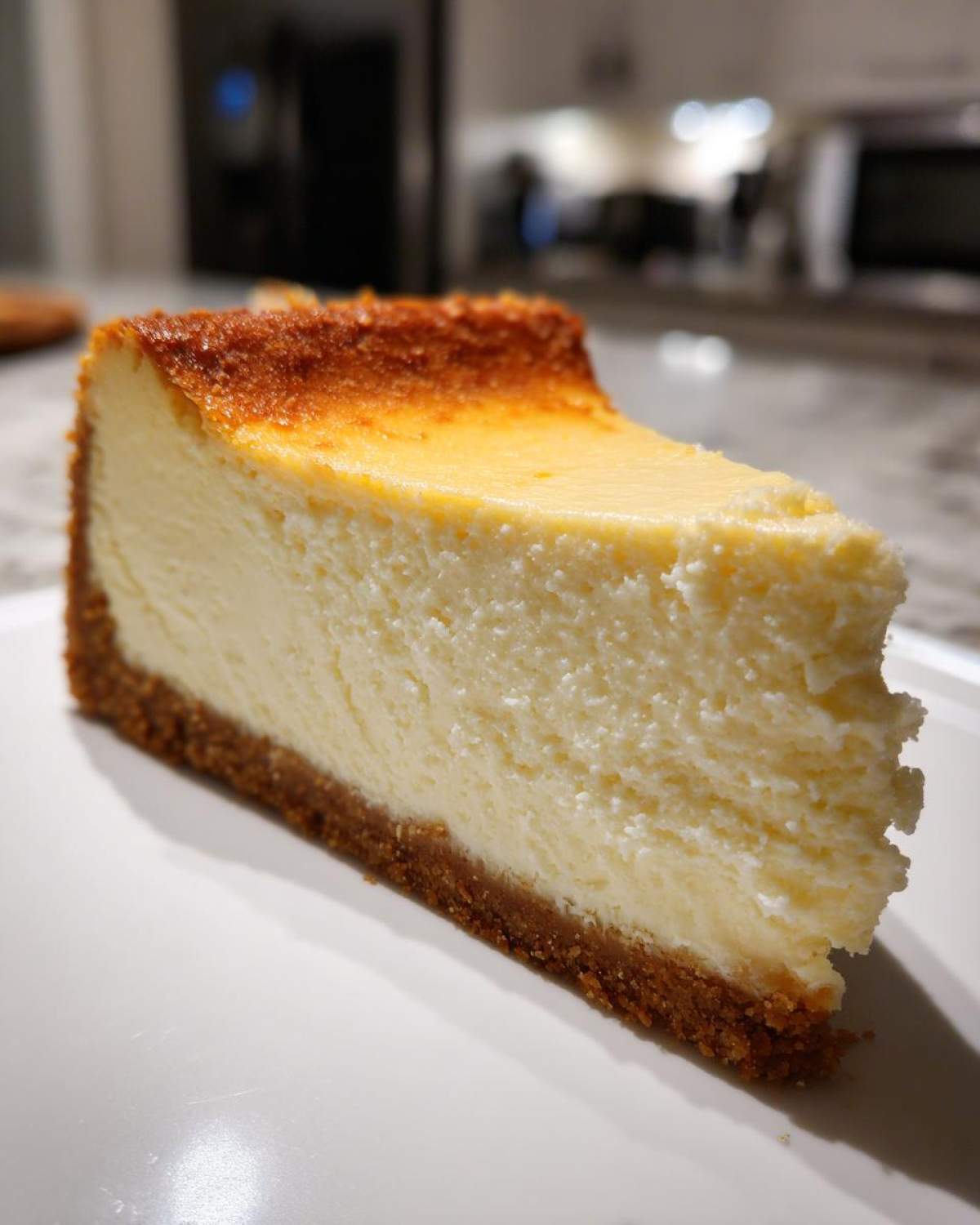 A close-up of a thick slice of baked cheesecake recipe with a golden-brown top and graham cracker crust.