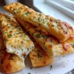 Close-up of cheesy Keto Garlic Breadsticks stacked on a white plate, showing a satisfying cheese pull.