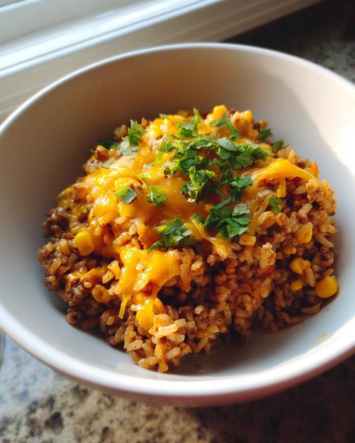 A serving of cheesy Mexican rice casserole topped with melted cheddar and fresh cilantro in a white bowl.