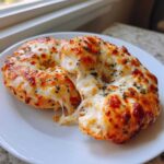 Two halves of freshly baked pizza bagels covered in melted, bubbly cheese and herbs, showing a dramatic cheese pull.