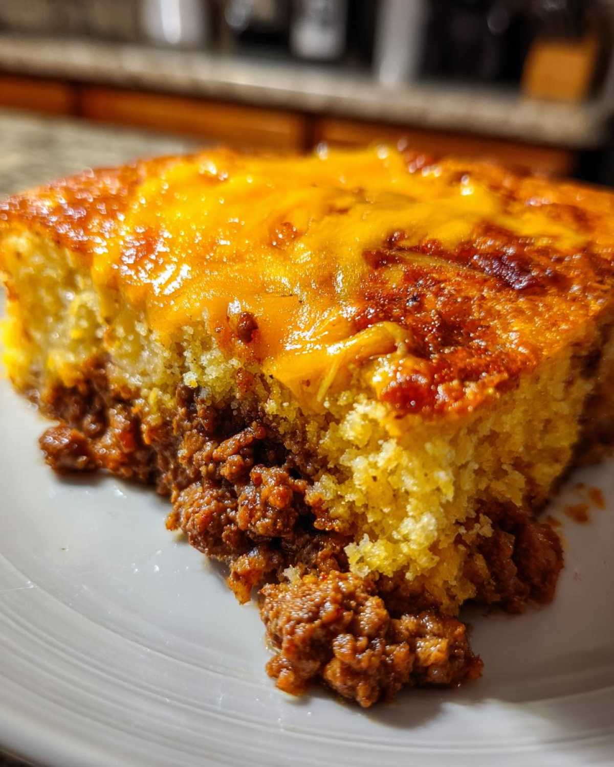 Close-up of a hearty slice of tamale pie showing a layer of seasoned ground meat topped with golden cornbread and melted cheddar cheese.
