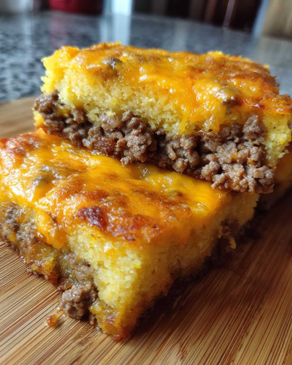 Two stacked squares of homemade tamale pie showing a layer of seasoned ground beef filling topped with melted cheddar cheese and cornbread.