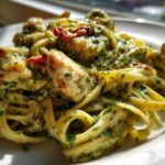 Close-up of creamy Chicken Pesto Pasta featuring fettuccine, chunks of chicken, and sun-dried tomatoes.