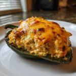 A close-up of a baked Chicken Stuffed Poblano Pepper topped with bubbly, melted, golden-brown cheese.