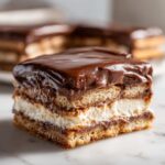 Close-up of a decadent slice of chocolate eclair cake showing layers of graham crackers, cream filling, and chocolate frosting.