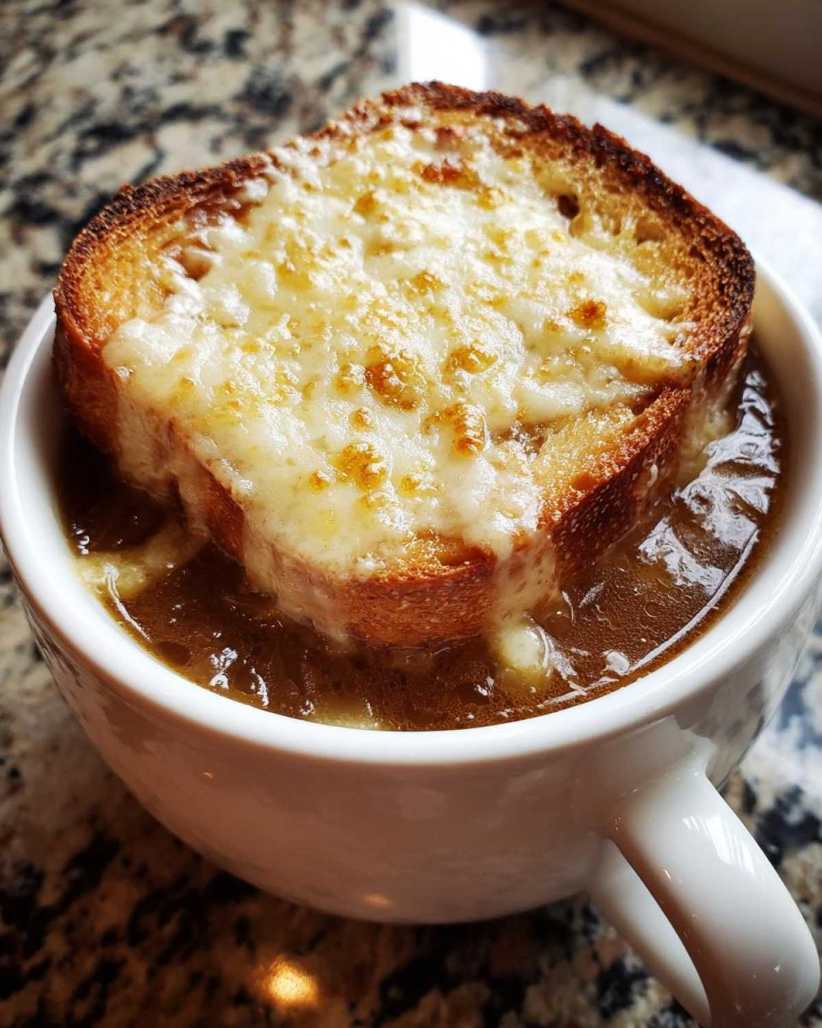 Close-up of a rich french onion soup topped with a thick slice of toasted bread and bubbly, melted Gruyère cheese.