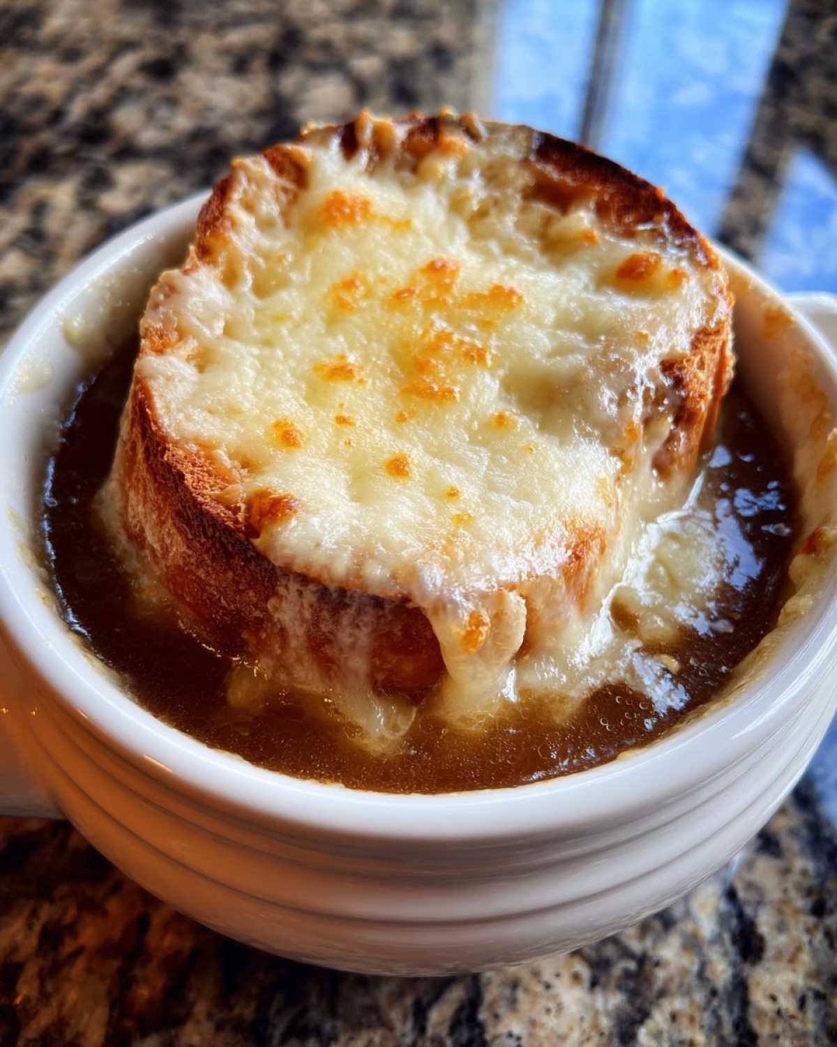 Close-up of a bowl of rich french onion soup topped with a thick, toasted crouton and bubbling, melted Gruyère cheese.