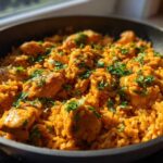 Close-up of vibrant, orange-hued Creamy Cajun Chicken Rice garnished with fresh parsley in a dark skillet.