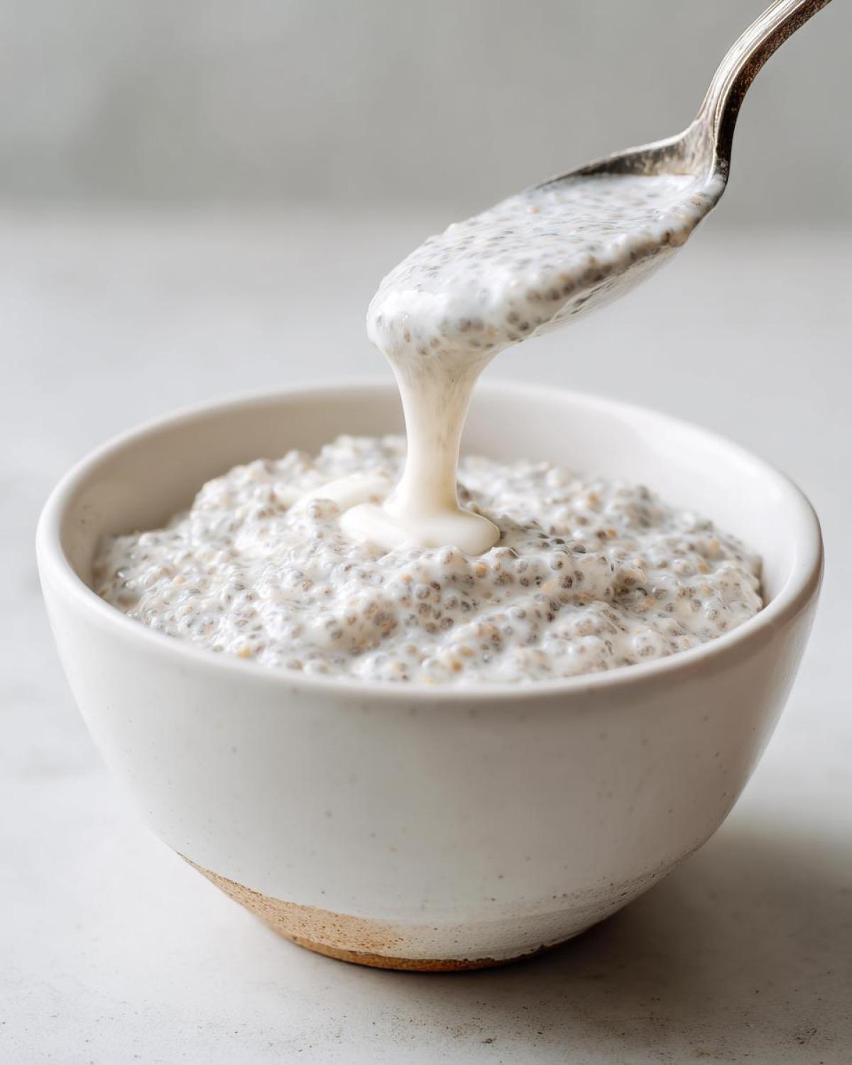 A spoonful of creamy coconut chia pudding is being lifted from a white bowl.