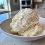 Two generous scoops of creamy, pale yellow cottage cheese ice cream served in a white bowl.
